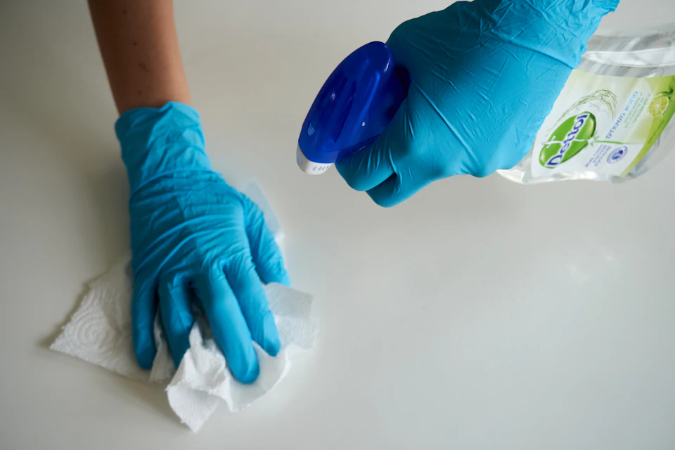 A person in blue gloves wiping a white surface with a paper towel