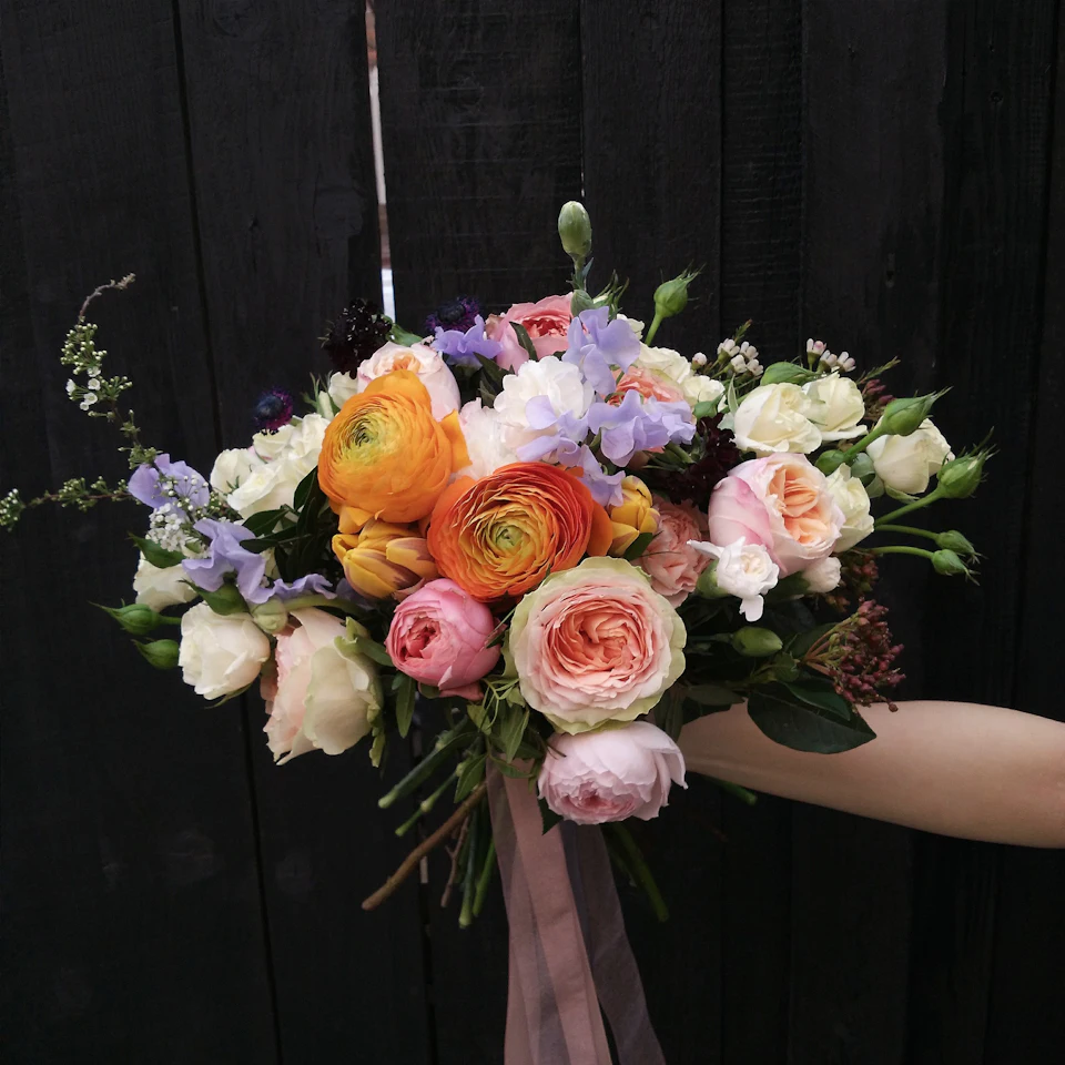A hand holds a vibrant bouquet of colorful flowers