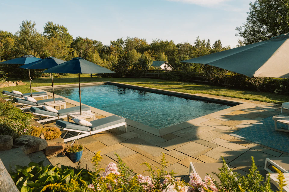 A swimming pool with lounge chairs and blue umbrellas on a stone patio